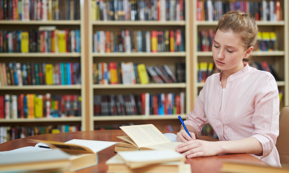 A young woman has multiple books open at a library