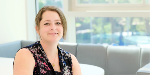 Image of a woman posing in front of a couch and window in a professional setting